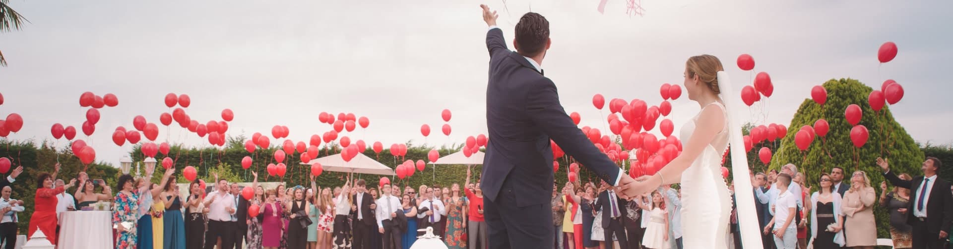 Wedding guests releasing red balloons at an outdoor celebration