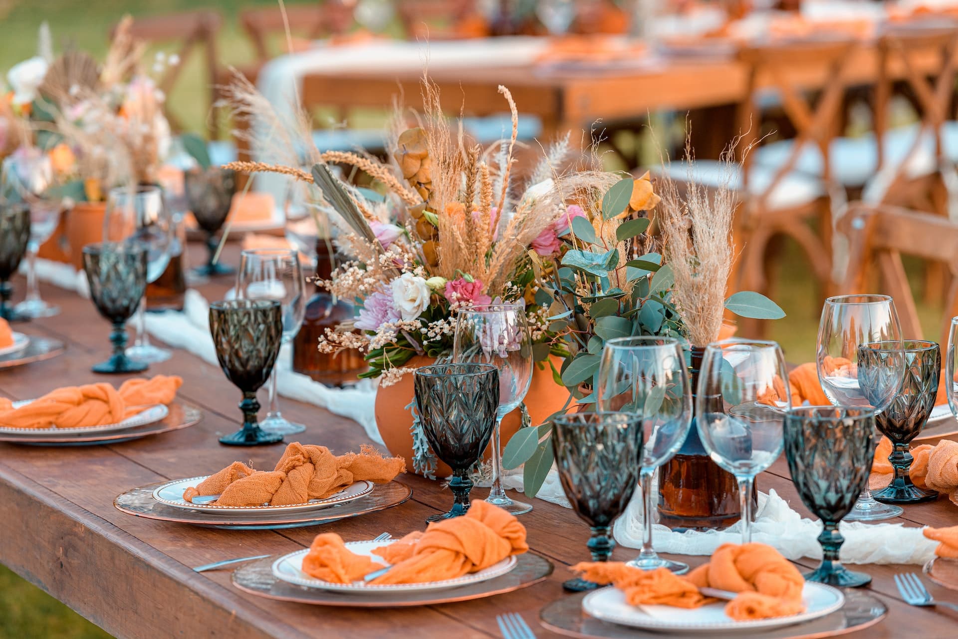 Outdoor wedding reception table with terracotta linens, floral centerpieces, and copper chargers